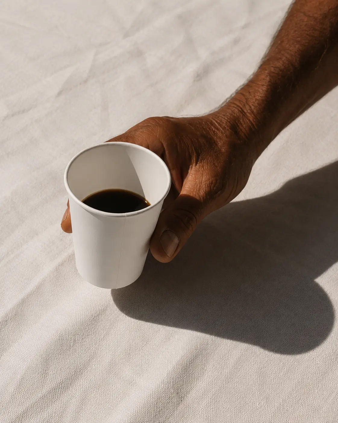 Hand holding a plain white paper cup of coffee