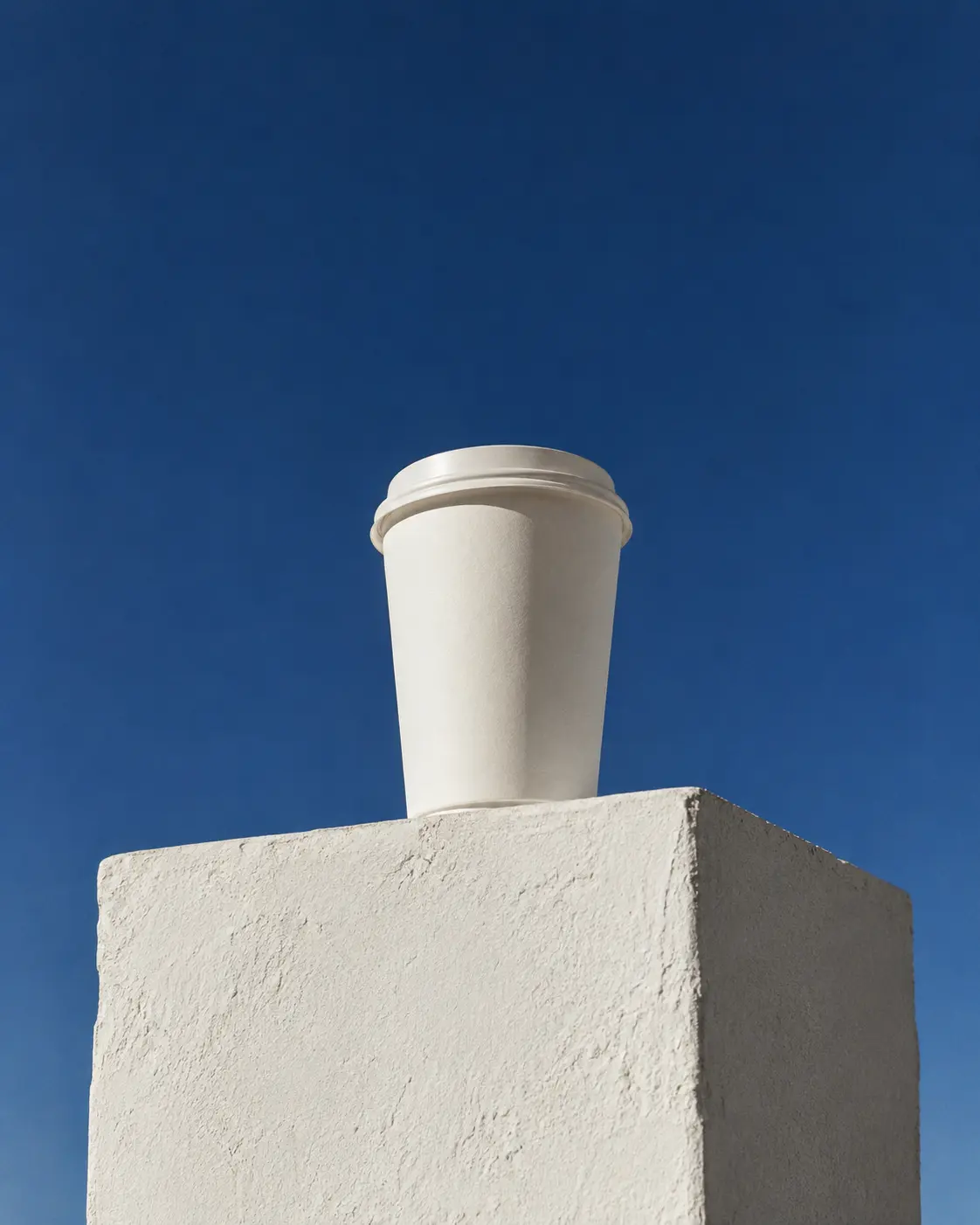 Plain white paper cup standing against a deep blue sky